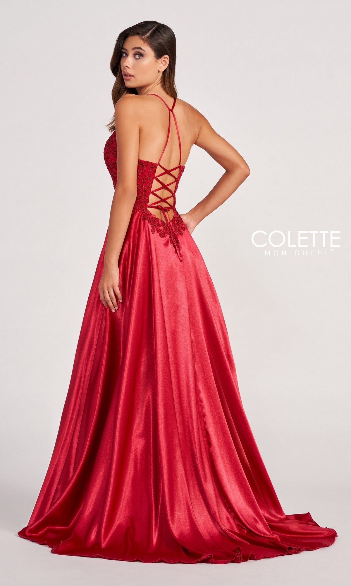 A woman models the Colette by Daphne Satin Prom Ball Gown CL2033, featuring a lace-up back and floral details, as she stands looking over her shoulder.